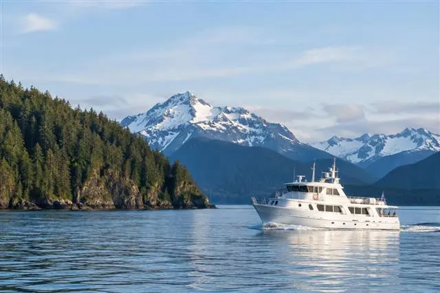Cruising the outer coast | Alaska Coastal Hunts White charter vessel cruising calm Alaskan coastal water past forested islands and snowy peaks
